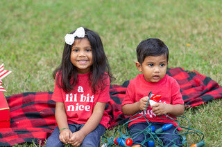 Two children sitting on plaid blanket wearing red bella+ canvas tee with white print says a lil bit nice
